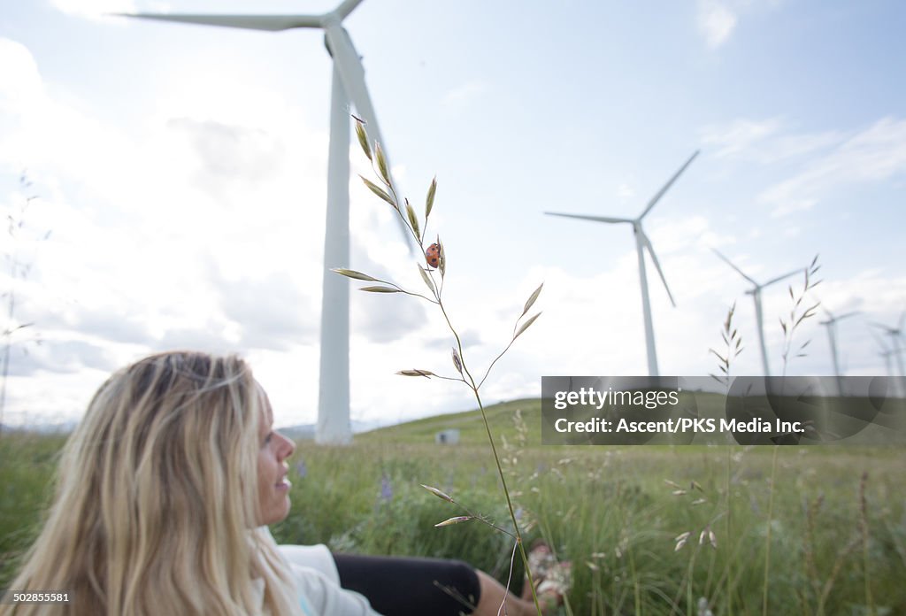 Woman relaxes in green meadow below wind turbines