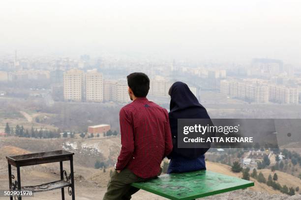 An Iranian couple look at a heavily polluted skyline as seen from western Tehran on December 30, 2015. Exhaust fumes from the five million cars and...