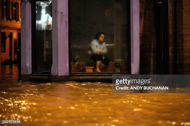 Woman sits inside a Chinese Restaurant watching floodwater race by the window in Dumfries, southern Scotland, on December 30, 2015 after heavy...