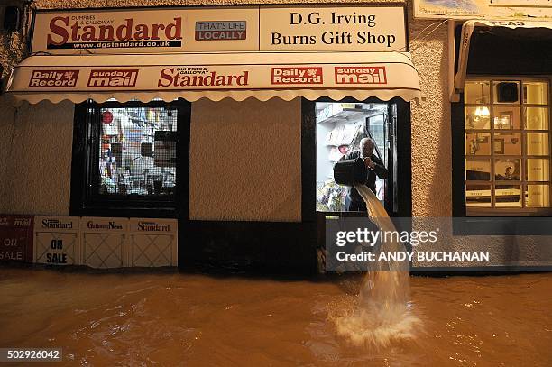 Shopkeeper Donald Irving bails floodwater out if his shop after the River Nith burst its banks in Dumfries, southern Scotland, on December 30, 2015...
