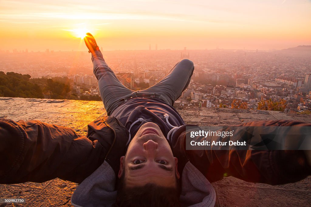 Guy taking a original selfie laying on the Barcelona bunkers (Turo de la Rovira) with the Barcelona cityscape on beautiful sunrise light.