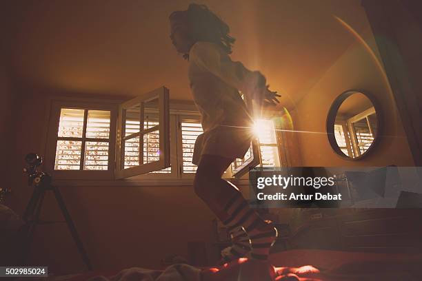 young girl jumping and playing on the bed with beautiful sunrise light through the window. - jump on bed photos et images de collection