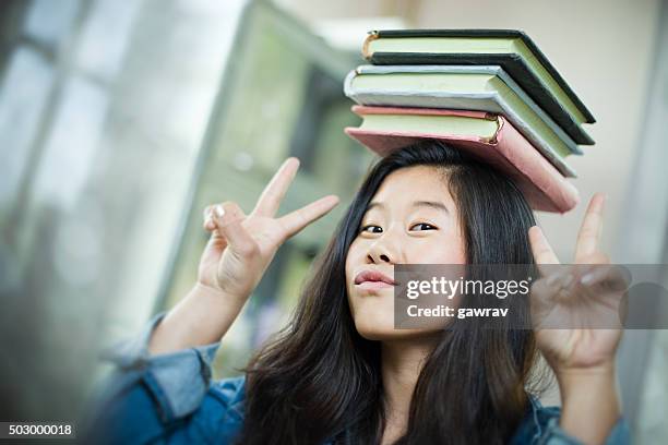 glücklich asiatische mädchen-student balancing stapel von büchern über kopf. - roman numeral stock-fotos und bilder