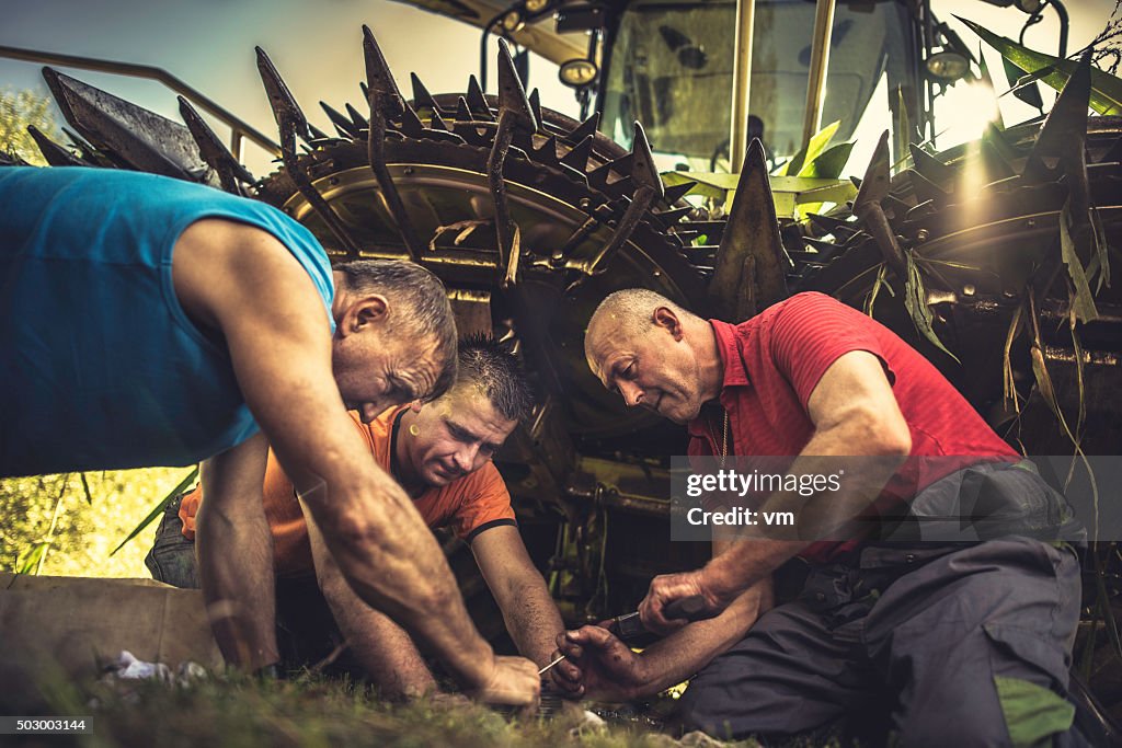 Three men kneeling by a combine harvester repairing it