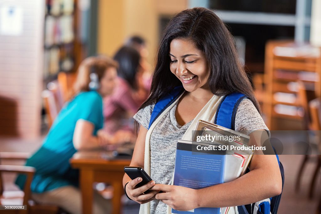 Student texting with smart phone in high school library