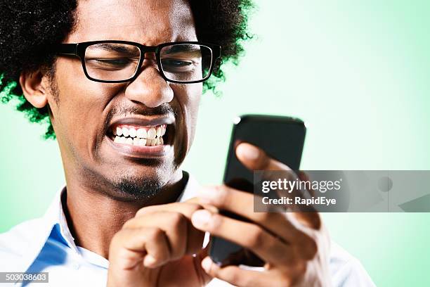 jeune afro-poil de nerd grimaces au téléphone portable qu'il détient - scientist mad photos et images de collection