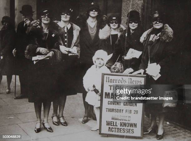 Advertising for a masked ball at Covent Garden by masked ladies in front of the luxury department store Harrods in London. About 1930. Photograph.