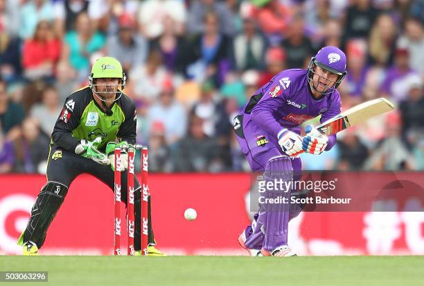 Ben Dunk of the Hurricanes bats as wicketkeeper Chris Hartley of the Thunder looks on during the Big Bash League match between the Hobart Hurricanes...