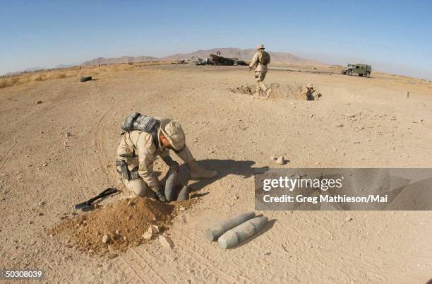 Navy Lt. Mike Runkle, assigned to Explosive Ordnance Disposal, Mobile Unit Two, Detachment-18 preparing charges to blow up stockpiled ordnance left...