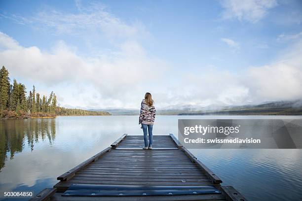 serene woman stands on pier relaxing by the lake - wood pier stock pictures, royalty-free photos & images