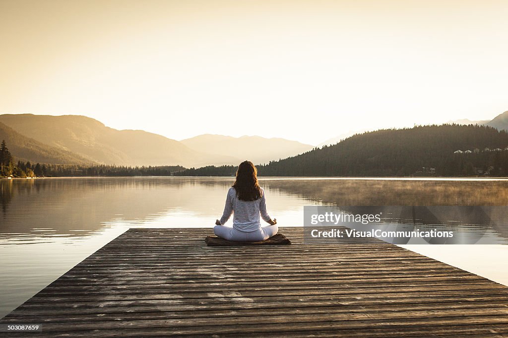 Woman meditating by lake.
