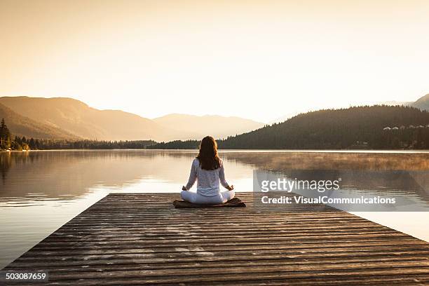 woman meditating by lake. - zen stock pictures, royalty-free photos & images