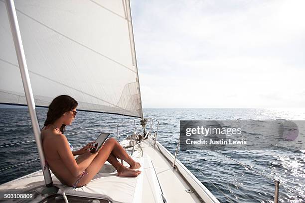 girl on tablet computer while sunbathing on front of sailboat - ships bow stock pictures, royalty-free photos & images