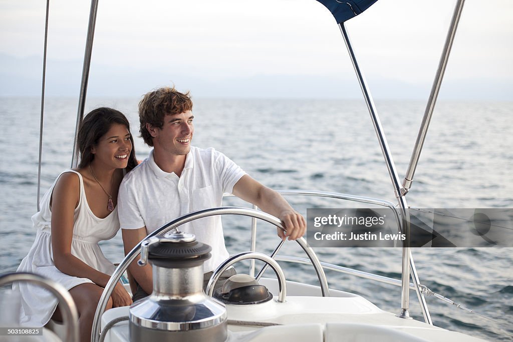 Couple steering a sailboat during sunset cruise