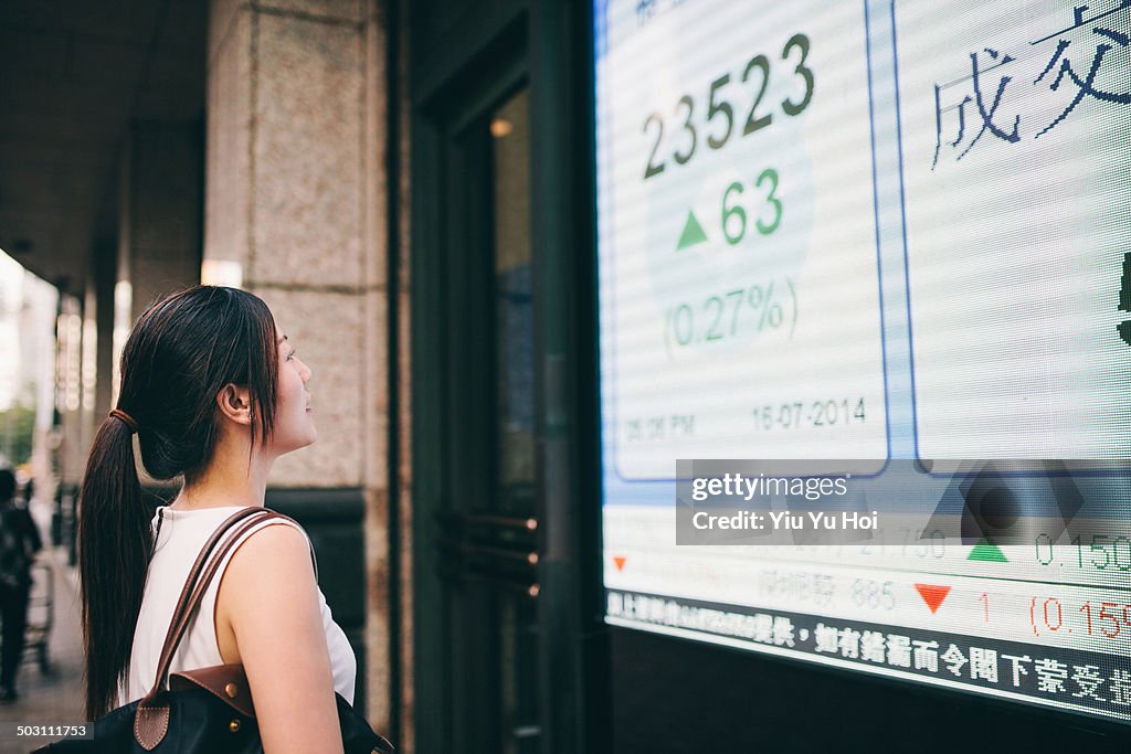 Asian businesswoman looking at stock quote board