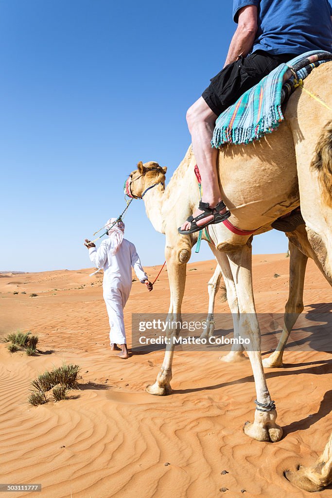 Bedouin leading a camel with tourist in the desert