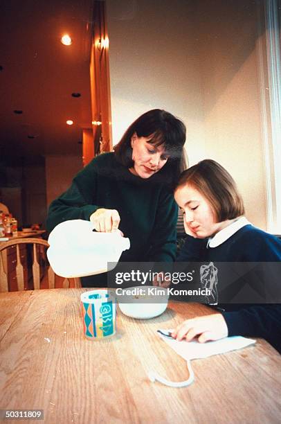 Author Dr. Nancy Snyderman pouring milk into cereal bowl as daughter Kate sits at kitchen table at home.