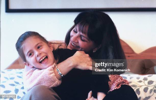 Author Dr. Nancy Snyderman embracing daughter Rachel as they sit on bed at home.