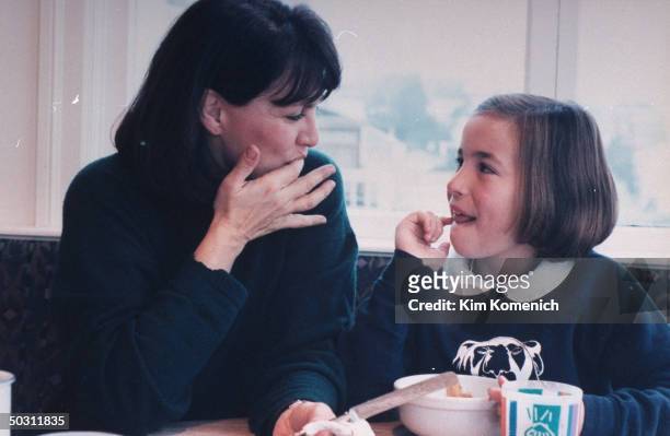 Author Dr. Nancy Snyderman & daughter Kate licking their fingers as they sit at kitchen table at home.