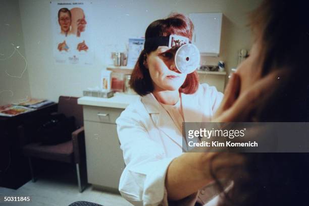Author Dr. Nancy Snyderman, sporting headband w. Attached medical examination light reflector on it, examining unident. Patient in her office.