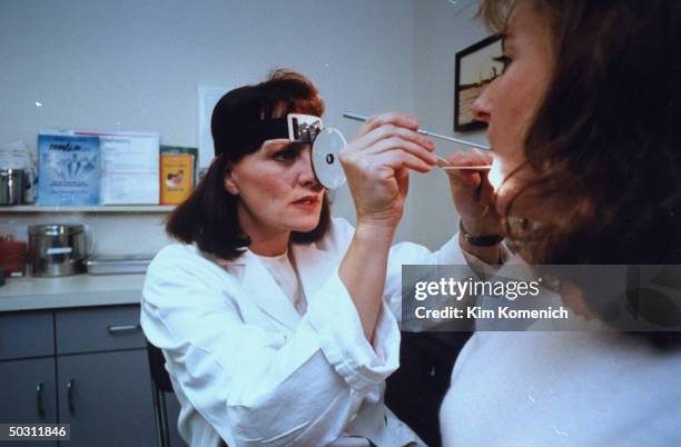 Author Dr. Nancy Snyderman, sporting headband w. Attached medical examination light reflector on it, examining unident. Patient in her office.