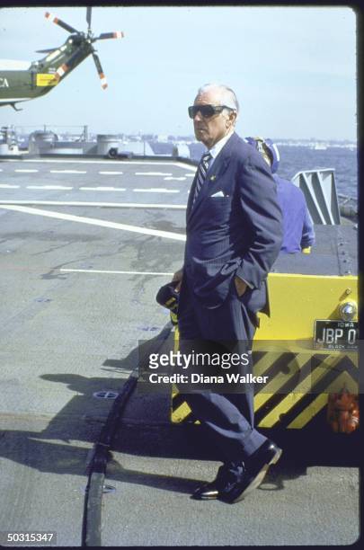Whitehouse Chief of Staff Donald T. Regan standing alone outside airport with tail of Marine One in background.