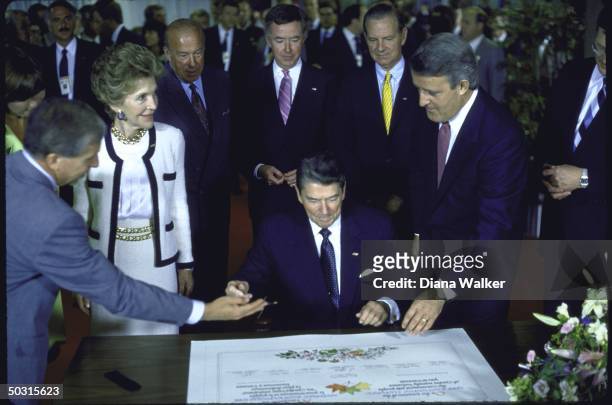 Pres. Ronald W. Reagan signing a document as wife Nancy , Canada's Prime Minister Brian Mulroney and US Secy of State George P. Shultz look on.