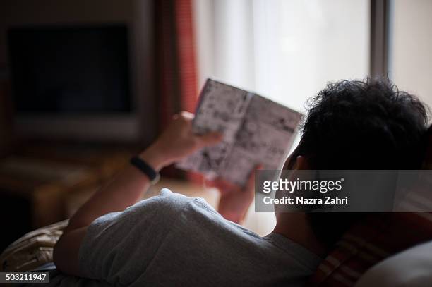 man reading manga comic at home - manga stock pictures, royalty-free photos & images