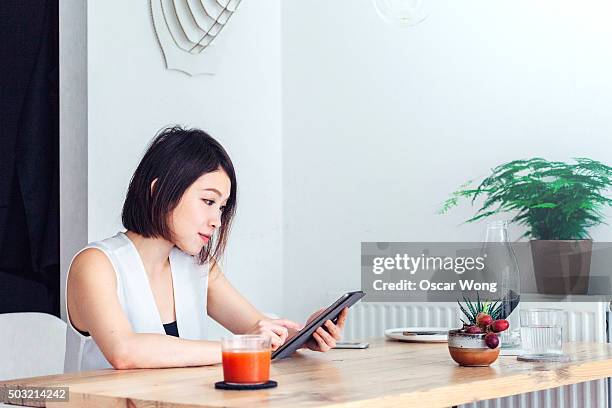 young woman reading news on tablet whilst having breakfast - center for asian american media stock pictures, royalty-free photos & images