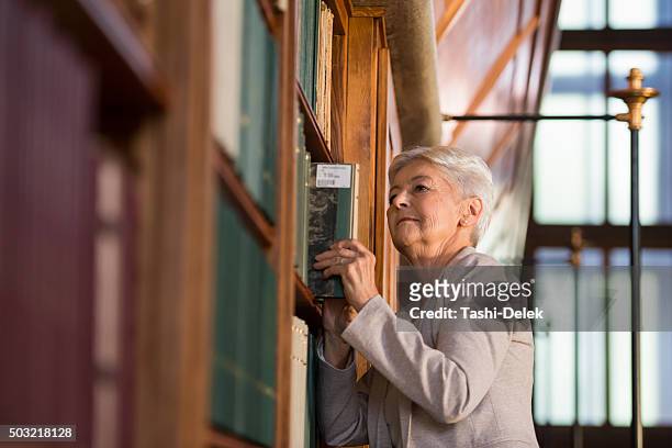 senior woman standing next to the bookshelves - librarian stock pictures, royalty-free photos & images