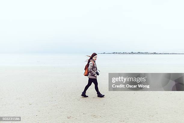 a young woman walking on the beach - windswept stock pictures, royalty-free photos & images