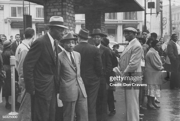 Group of African Americans including Rev. Martin Luther King waiting at busy bus stop following Supreme Court ruling ending successful 381 day...