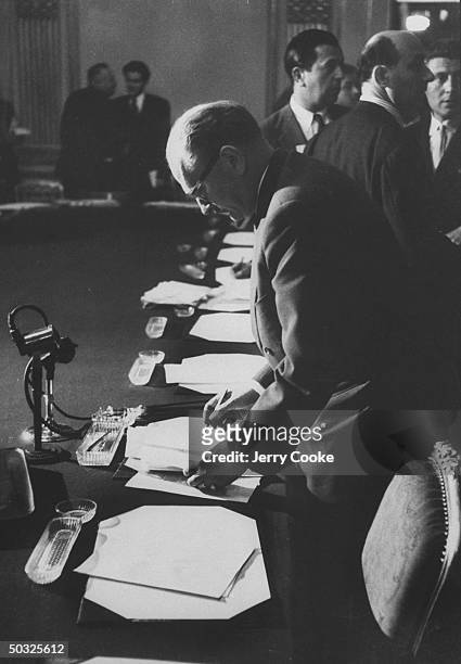 Guy Mollet writing on papers at the conference microphone during the Suez Crisis.