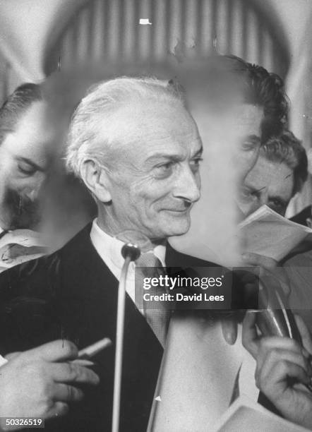 Italian Prime Minister Antonio Segni standing at the microphone while being surrounded by newsmen also holding up microphones.