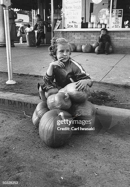 Chamber of commererce handed out free pumpkins for Holloween, this little girl guarding hers while her girl friend telephones mother to help lug them...