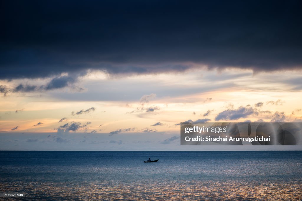 A lone fisherman on a boat under twilight sky.