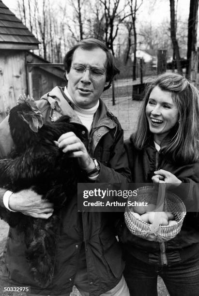 Publisher Andy Stewart holding a black Cochin hen and wife, caterer Martha, holding a basket of eggs in barnyard of their home.