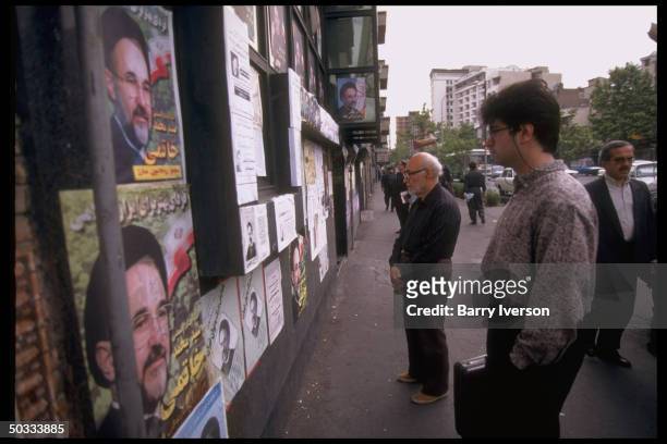 Pedestrians stopping for informative look at wall plastered w. Presidential election campaign posters picturing moderate cleric Mohammed Khatami,...
