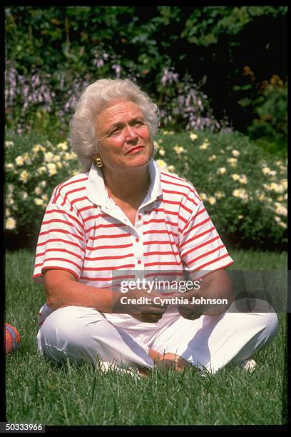 Would-be First Lady Barbara Bush sitting cross-legged on lawn of Bush home at Naval Observatory.
