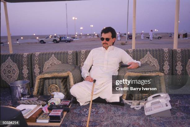 Billionaire investor Saudi Prince Alwaleed watching TV, remote control in-hand, by sunset at his weekend desert retreat 45 miles from Riyadh.