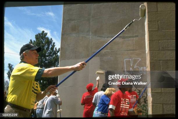 Pres. Bill Clinton joining youthful volunteers in painting over graffiti-marred wall during White House volunteerism agenda event at Marcus Foster...