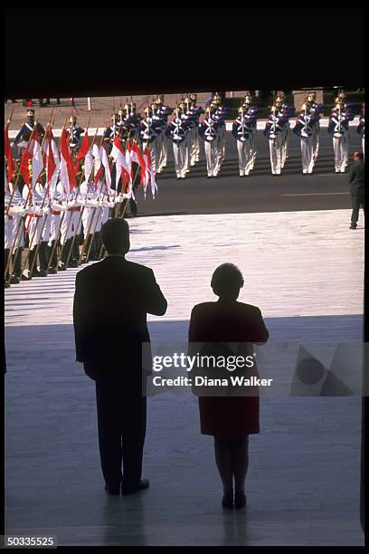 Pres. Bill Clinton & State Secy. Madeleine Albright poised w. Hands over hearts, in semi-silhouette, facing ceremonial troops during playing of natl....