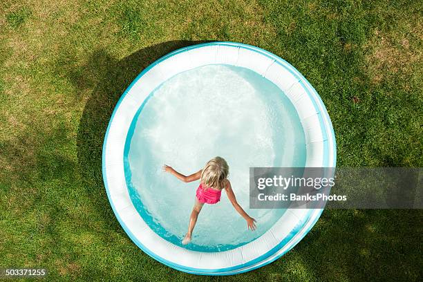 girl jumping into inflatable swimming pool, summer on dried grass - plastic pool stockfoto's en -beelden