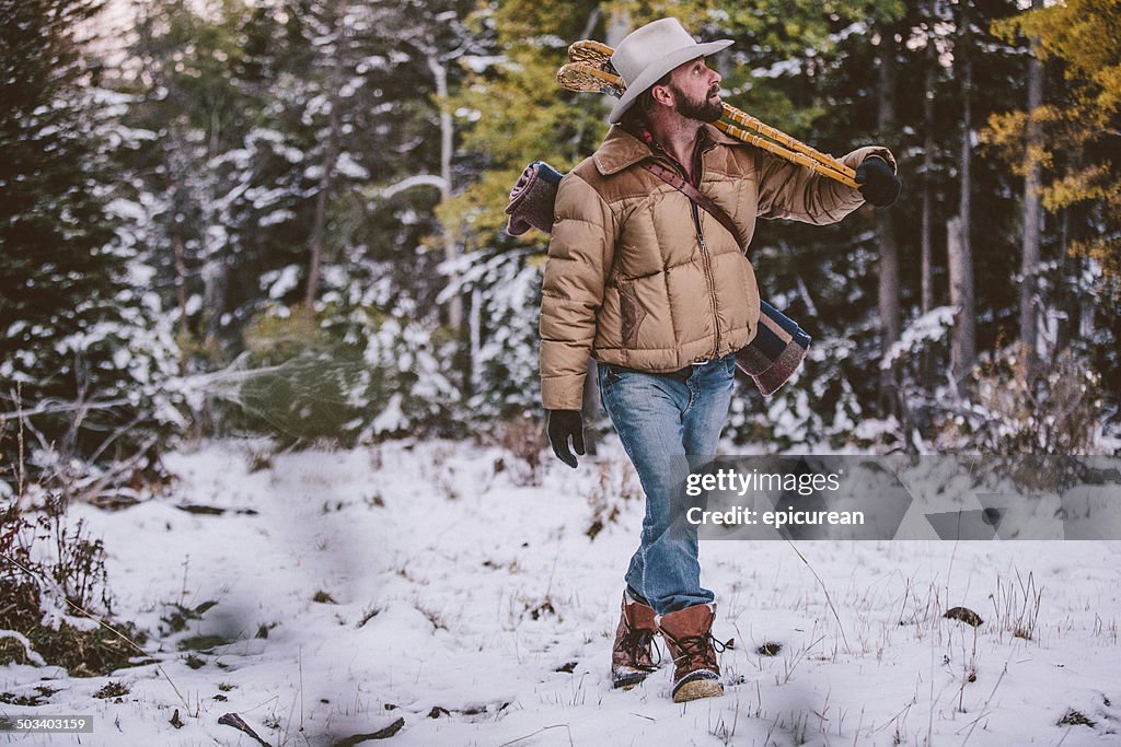 Man carries snowshoes over shoulder while walking through snowy woods