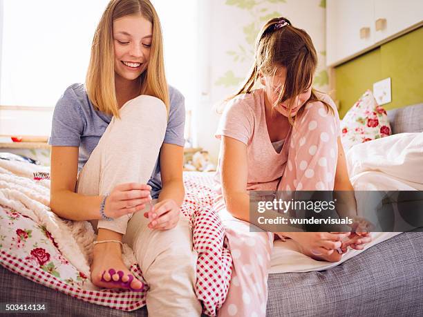 adolescent girls in pyjamas on bed painting their toenails together - teen girls toes stock pictures, royalty-free photos & images