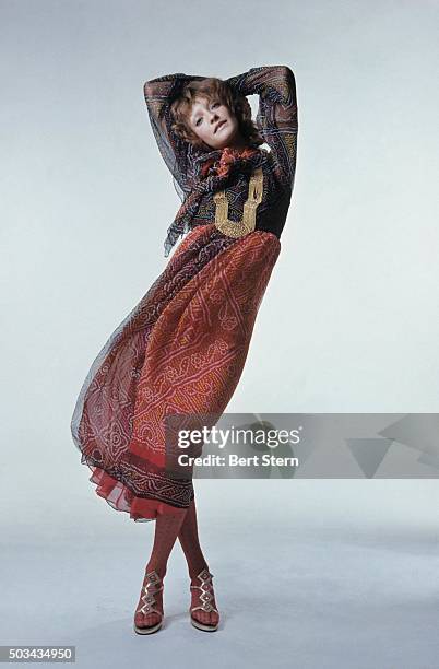 Model Loulou de la Falaise with arms overhead wears a printed chiffon peasant dress with jewelry by Surgit and Adarsh Gill for Saz with David Evins...