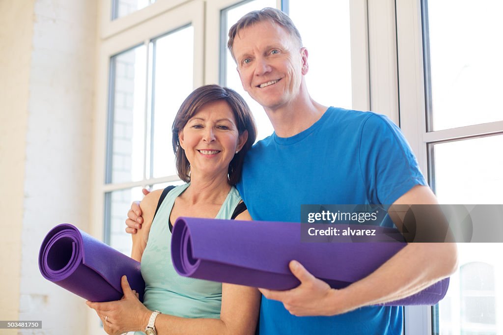 Happy mature couple standing with yoga mats