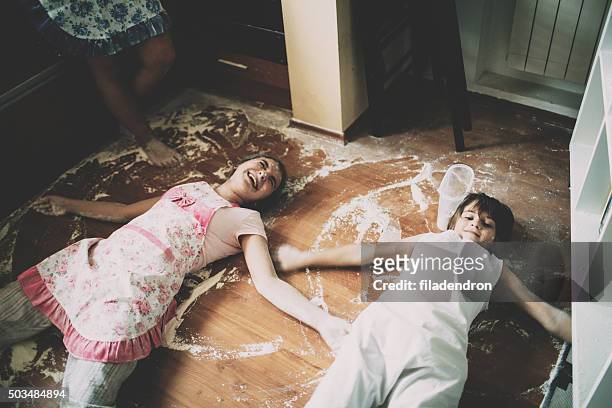 two children lying on floor in kitchen - kids mess stockfoto's en -beelden