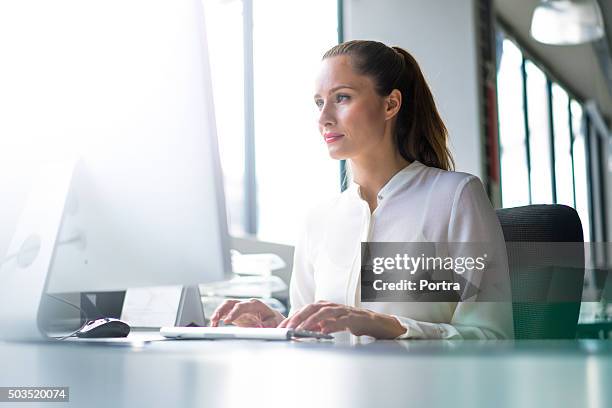 businesswoman using computer at desk in office - brightly lit office stock pictures, royalty-free photos & images