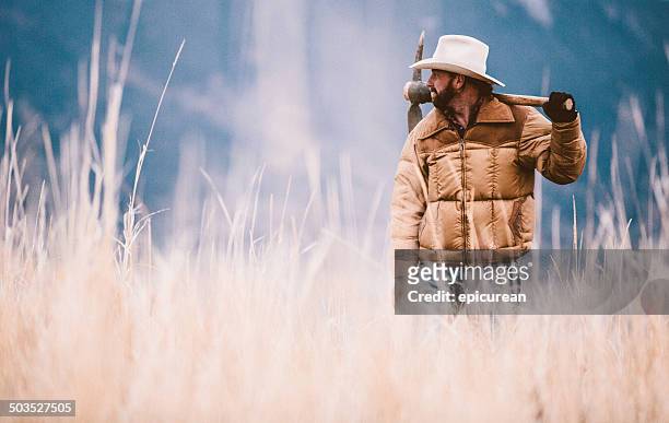 cowboy carrying pickaxe stands in valley of hay near mountains - pickaxe bildbanksfoton och bilder